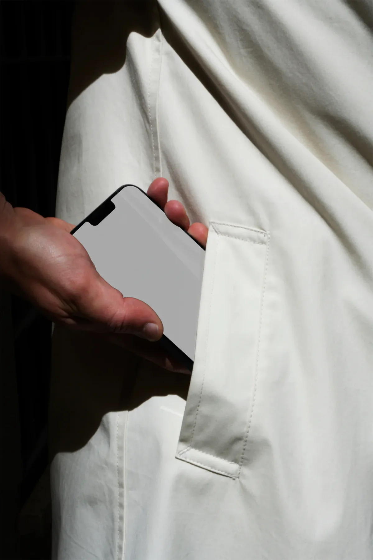 Hand holding an iPhone with a minimal black and white interface, partially in the pocket of a white coat, emphasizing clean design.