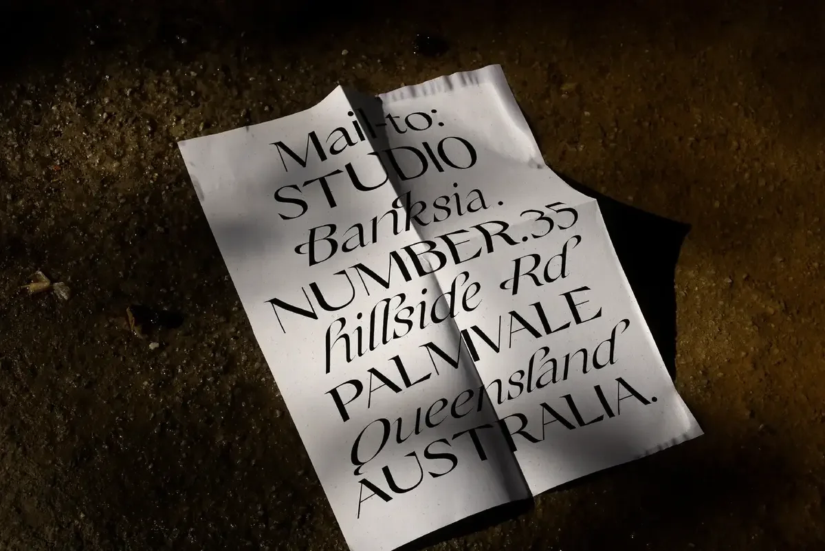 Crumpled paper featuring an elegant address in calligraphy: Mail-to: Studio Banksia, Number.35 Hillside Rd, Palmvale, Queensland, Australia.
