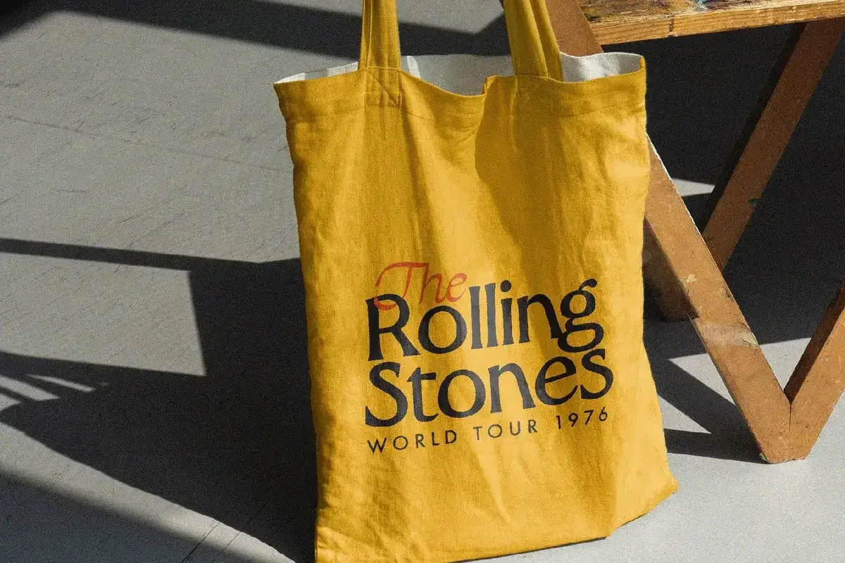 Yellow tote bag with "The Rolling Stones World Tour 1976" text in bold black and red, promoting a vintage rock and roll aesthetic.