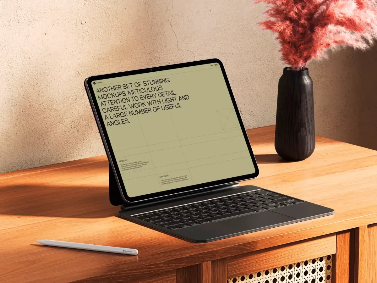 An iPad mockup with a keyboard and a stylus, displayed on a wooden table beside a vase with pink pampas grass, showcasing a design mockup in a minimalist interface.